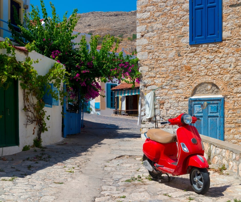 Czerwony skuter w wąskiej uliczce na tle kamiennych budynków, Chalki, Rodos, Grecja